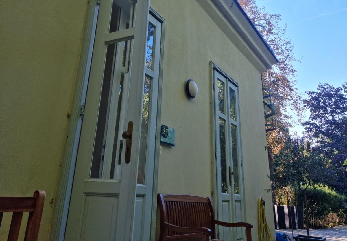 Die Eingangstür vo  Seminargebäude steht offen. Vor dem Gelben Haus stehen Sitzbänke aus Holz. Der Himmel ist blau.